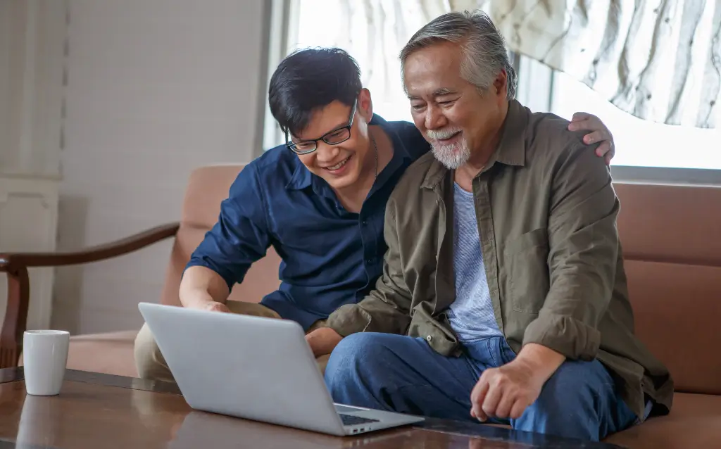 Adult son and aging father looking at a laptop together to research trusted senior living options