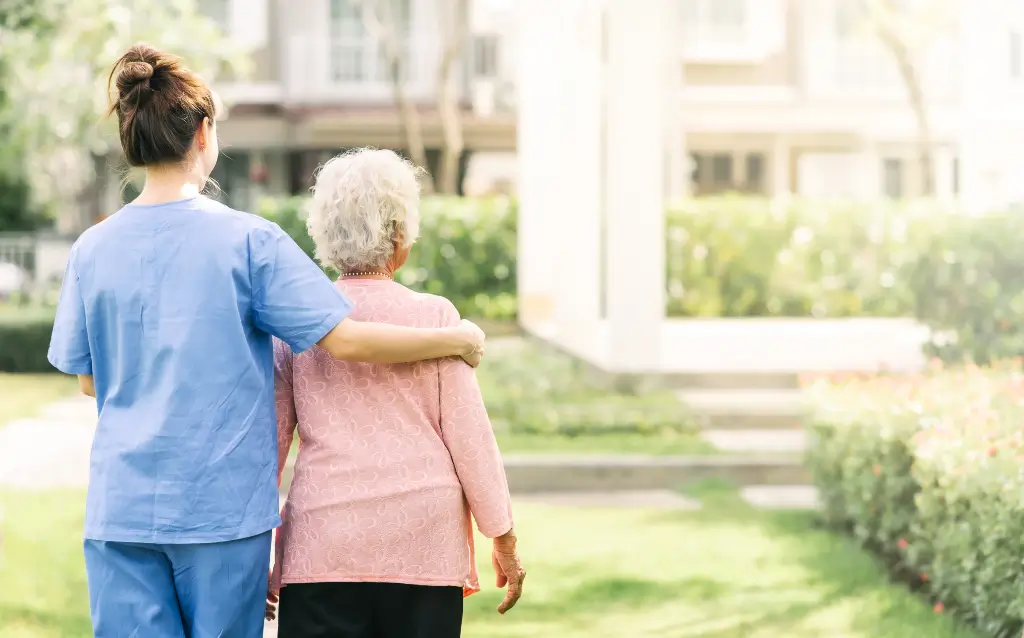 Senior care provider gently guiding an elderly woman on a walk outdoors