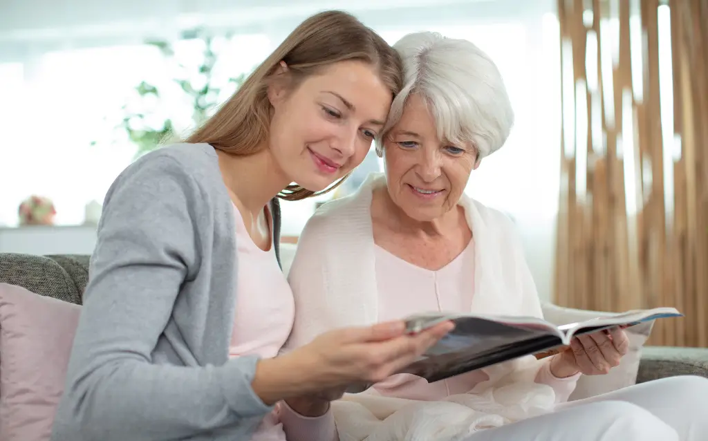 Daughter and elderly mother reading a magazine together, representing compassionate and personalized senior support