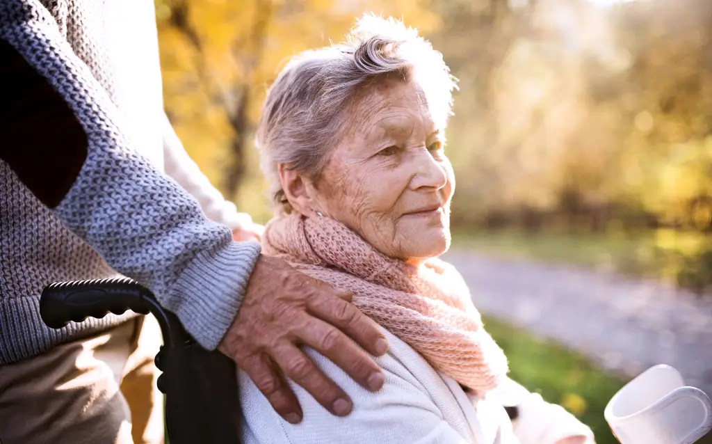 Compassionate caregiver placing a reassuring hand on the shoulder of an elderly woman in a wheelchair outdoors